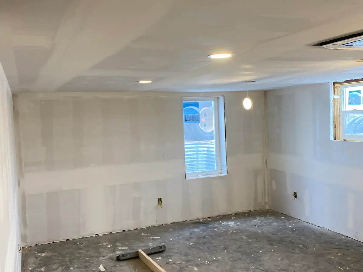 Room with installed drywall, taped joints, recessed ceiling lights and an unfinished floor.