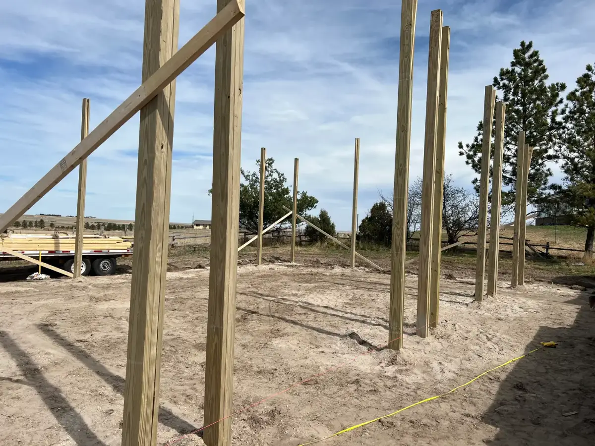 Tall timber posts supported by diagonal braces along the edge of a prepared building site.