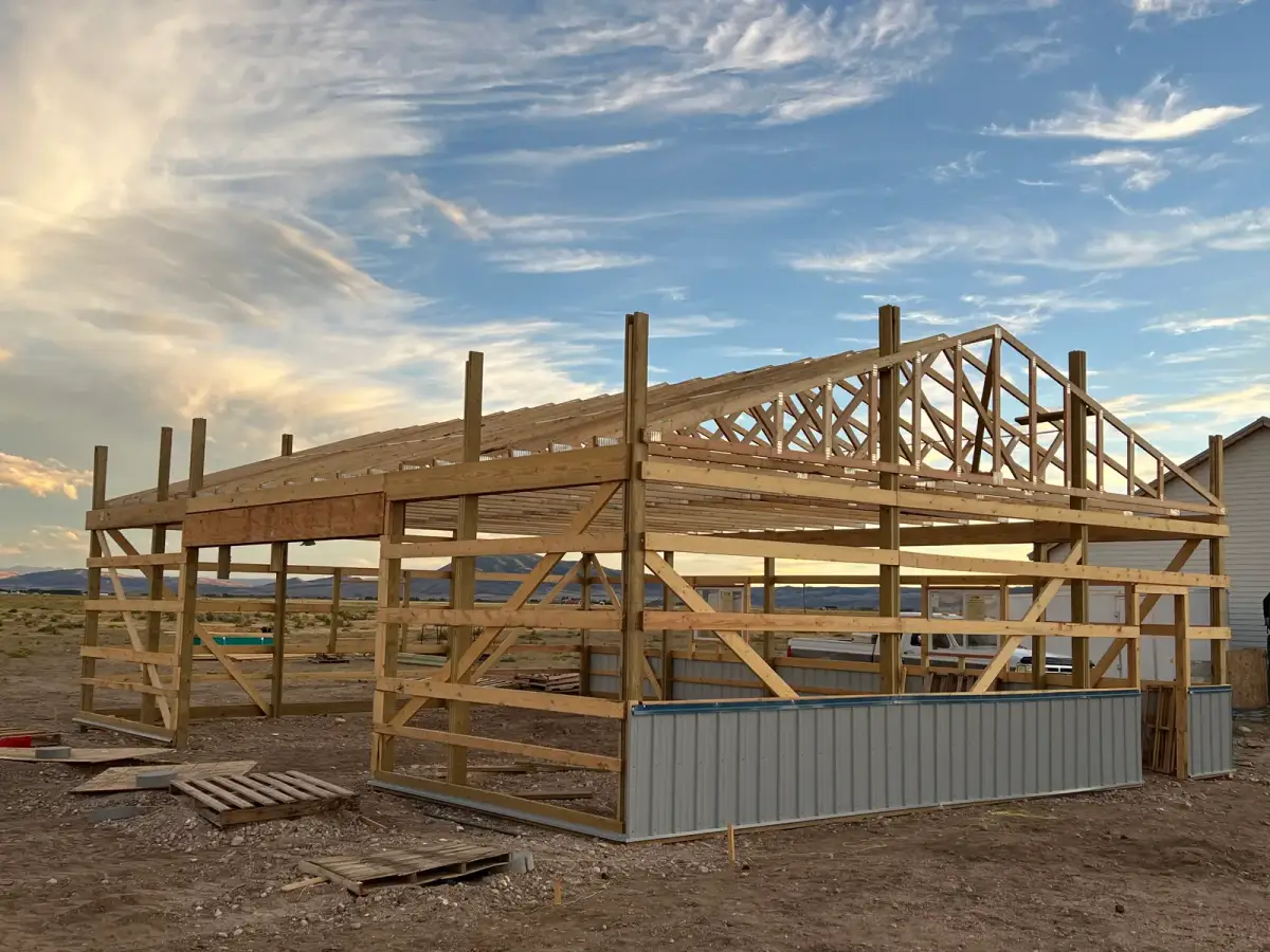 Timber posts and roof trusses on a partially clad building beneath an evening sky.
