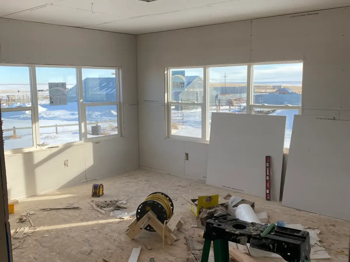 Room with new drywall, several windows and carpentry tools on the unfinished floor.