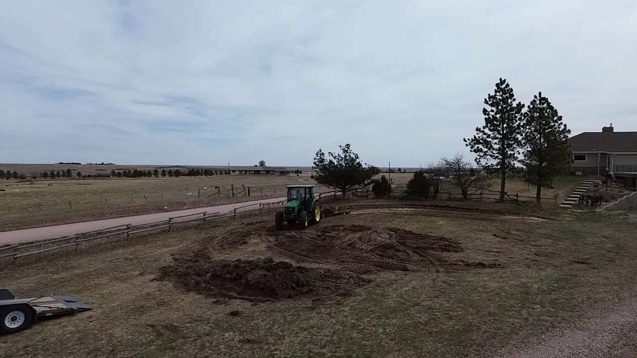 A tractor preparing a building site beside a house and trees.