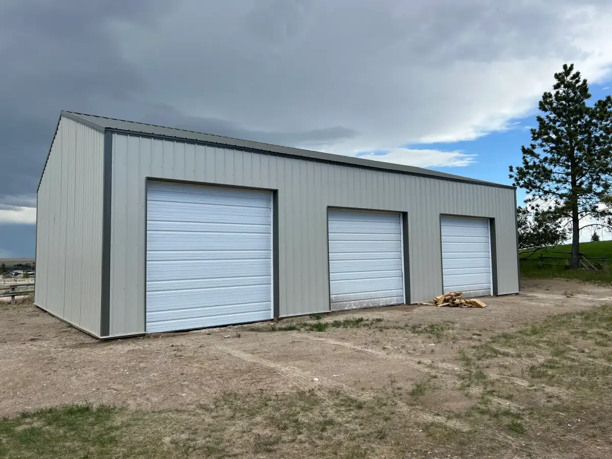 Light-colored metal garage with three white overhead doors and dark trim.